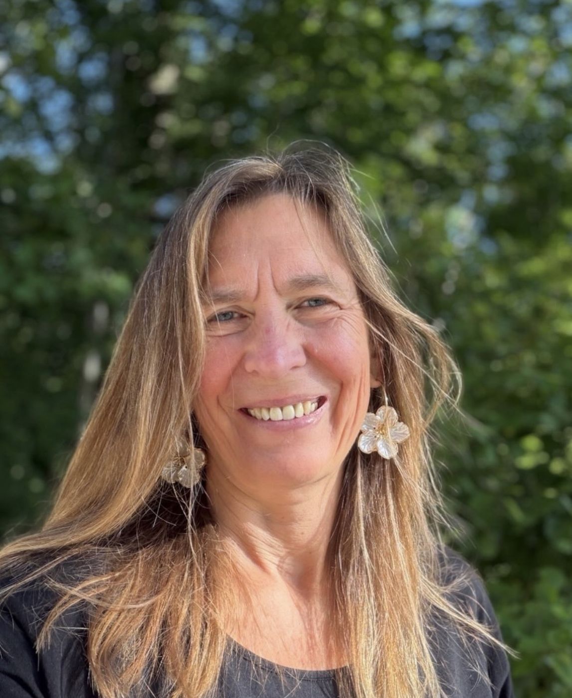 Sabine Ryan lächelt im Freien vor grünen Bäumen